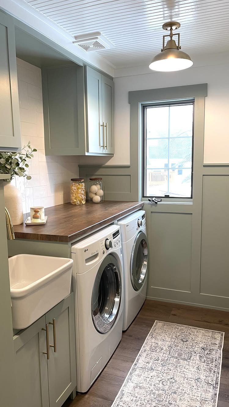 Sage green laundry room with white appliances, wooden counters, and board and batten wainscoting.
