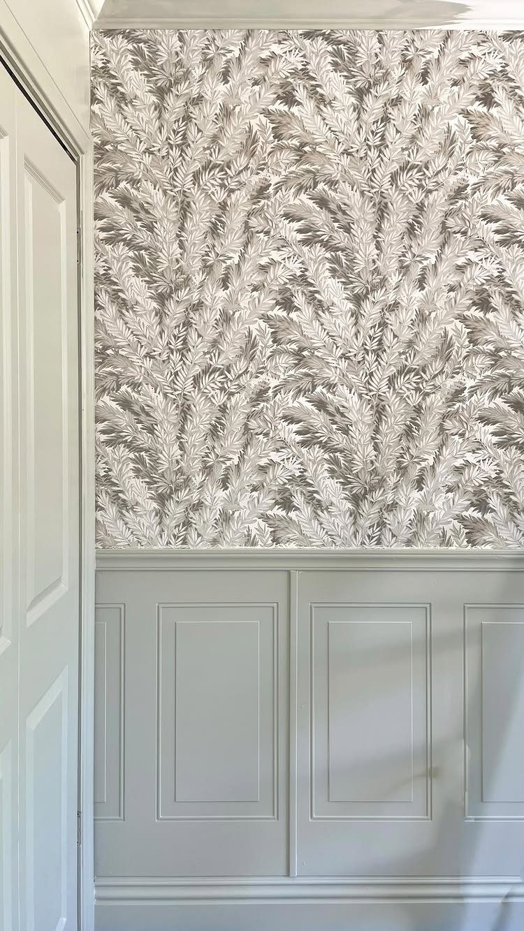 Grey paneled wainscoting installed below a white and grey botanical patterned wallpaper.