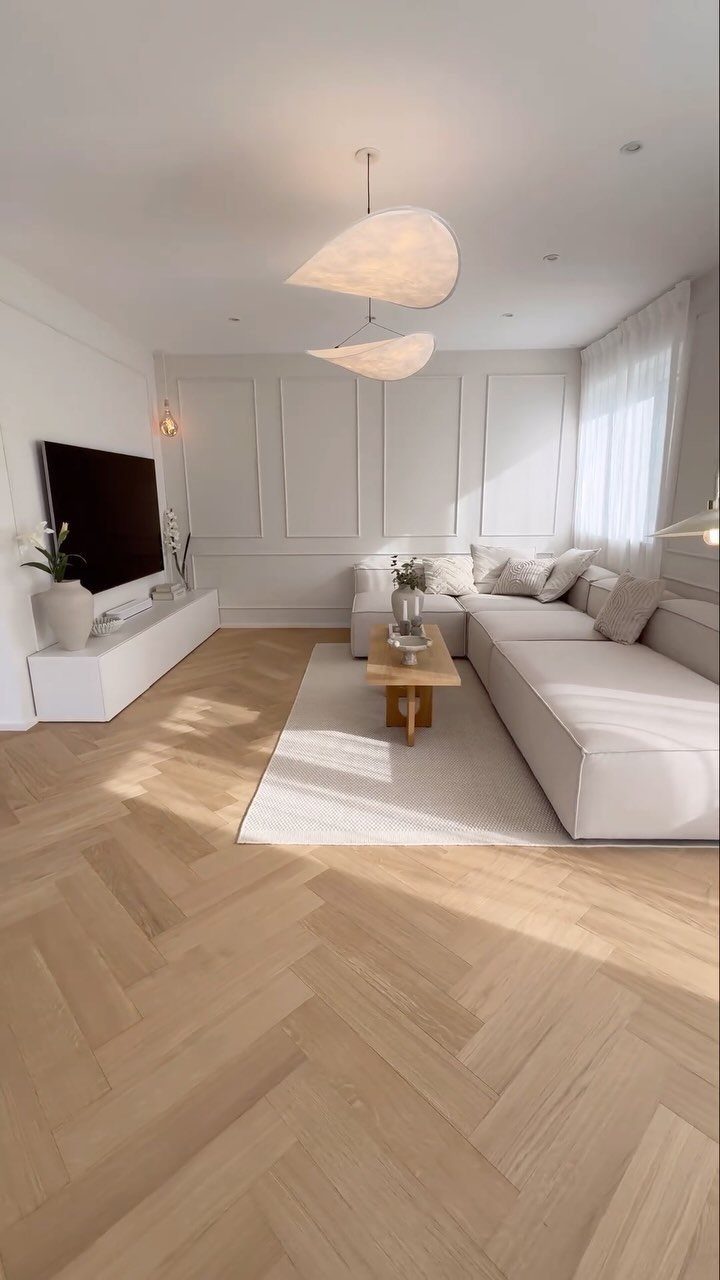 Light wood herringbone pattern flooring in a bright, modern living room with white furniture.