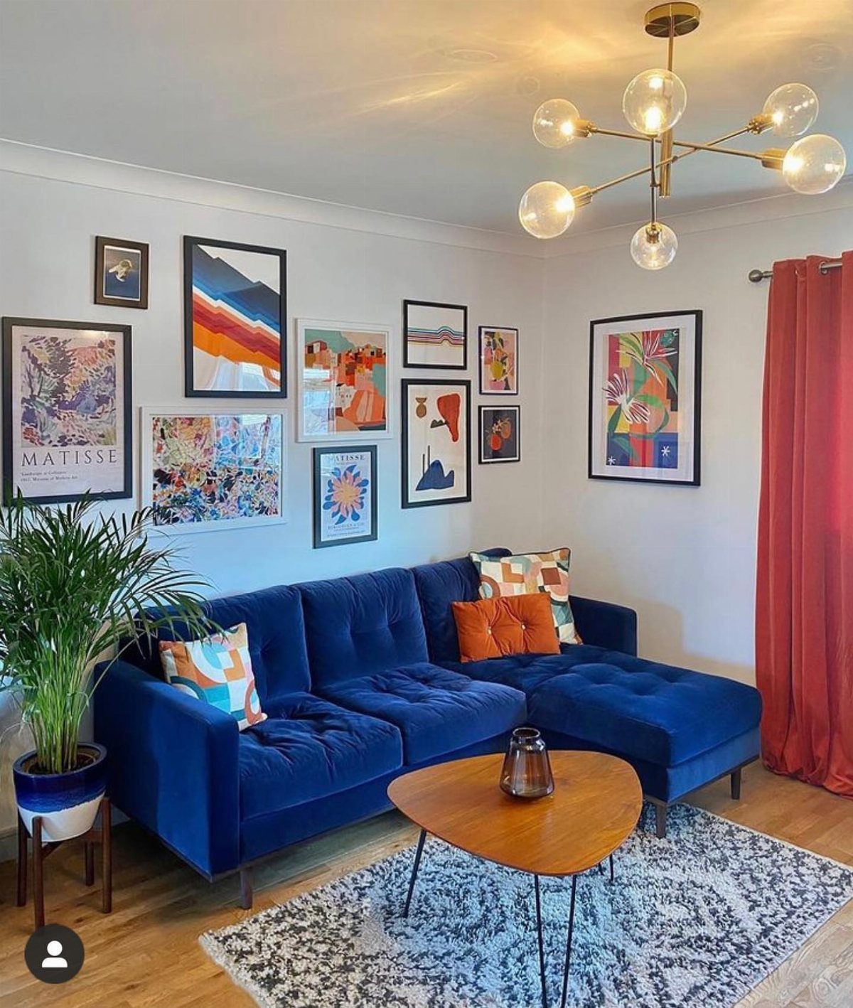 Framed colorful art pieces arranged in a gallery wall above a blue velvet sofa.