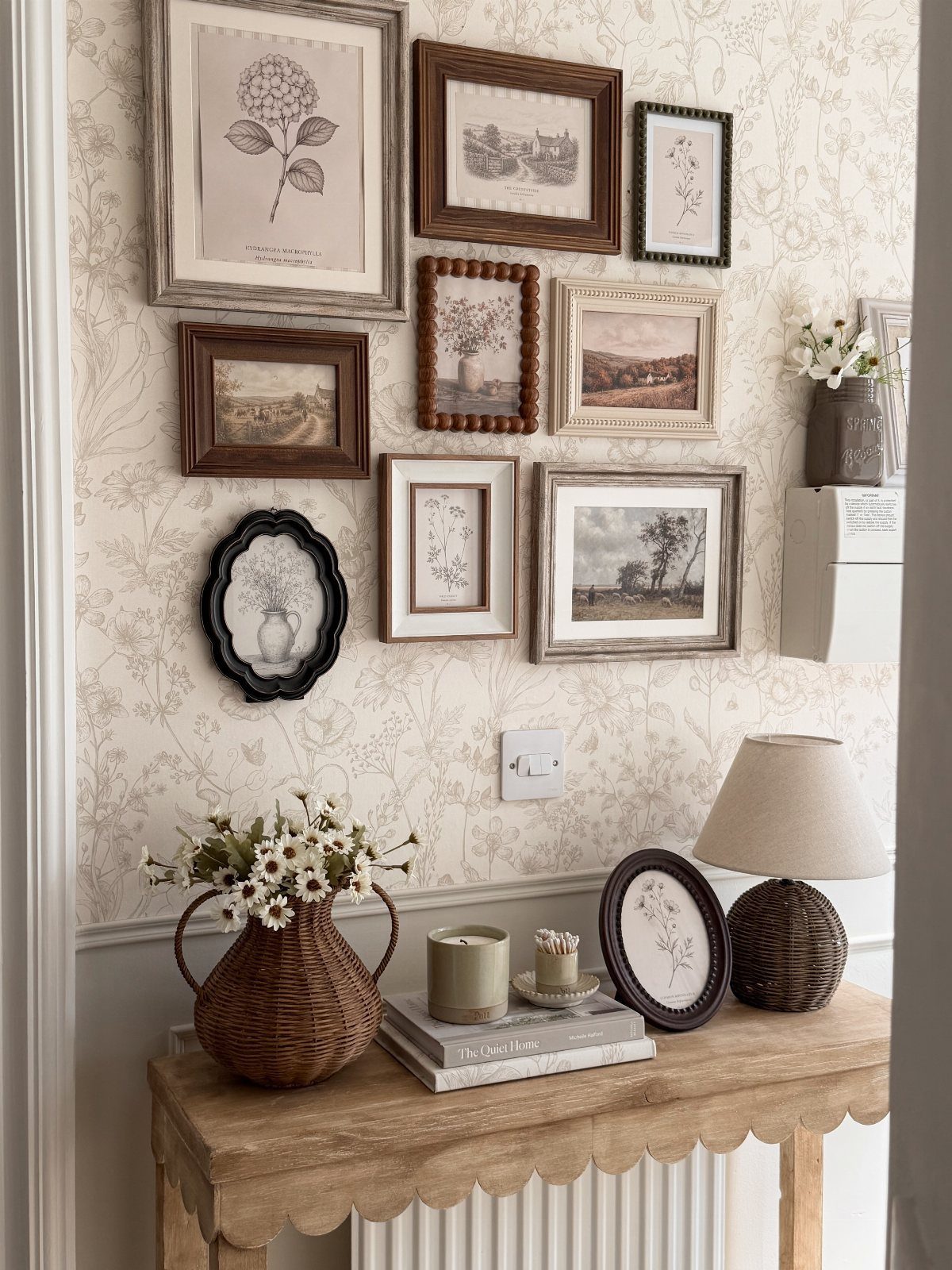 Framed botanical and landscape art pieces arranged on a patterned wall above a wooden console table.