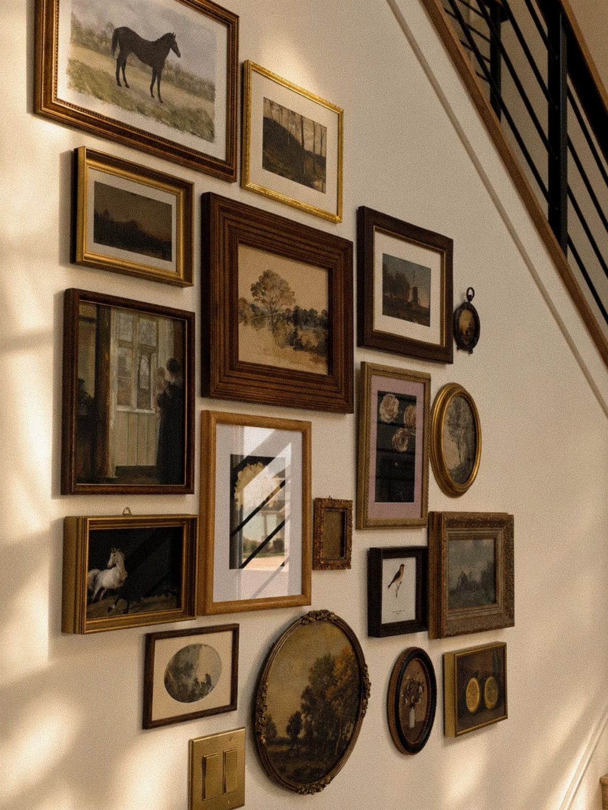 Assorted framed paintings and sketches arranged in a gallery wall layout on a white wall.