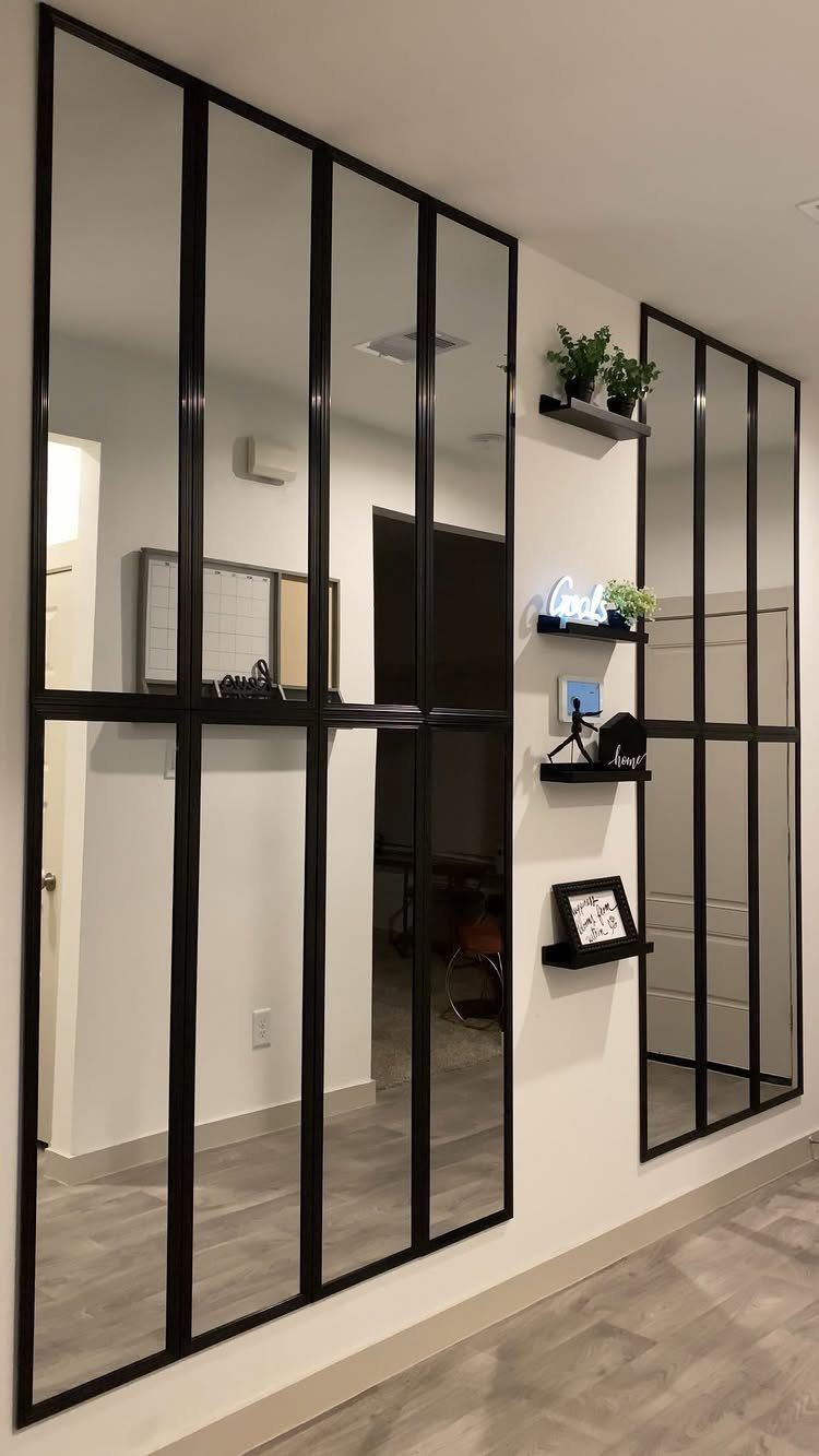 Large black paneled mirrors mounted on a white hallway wall with small floating shelves.