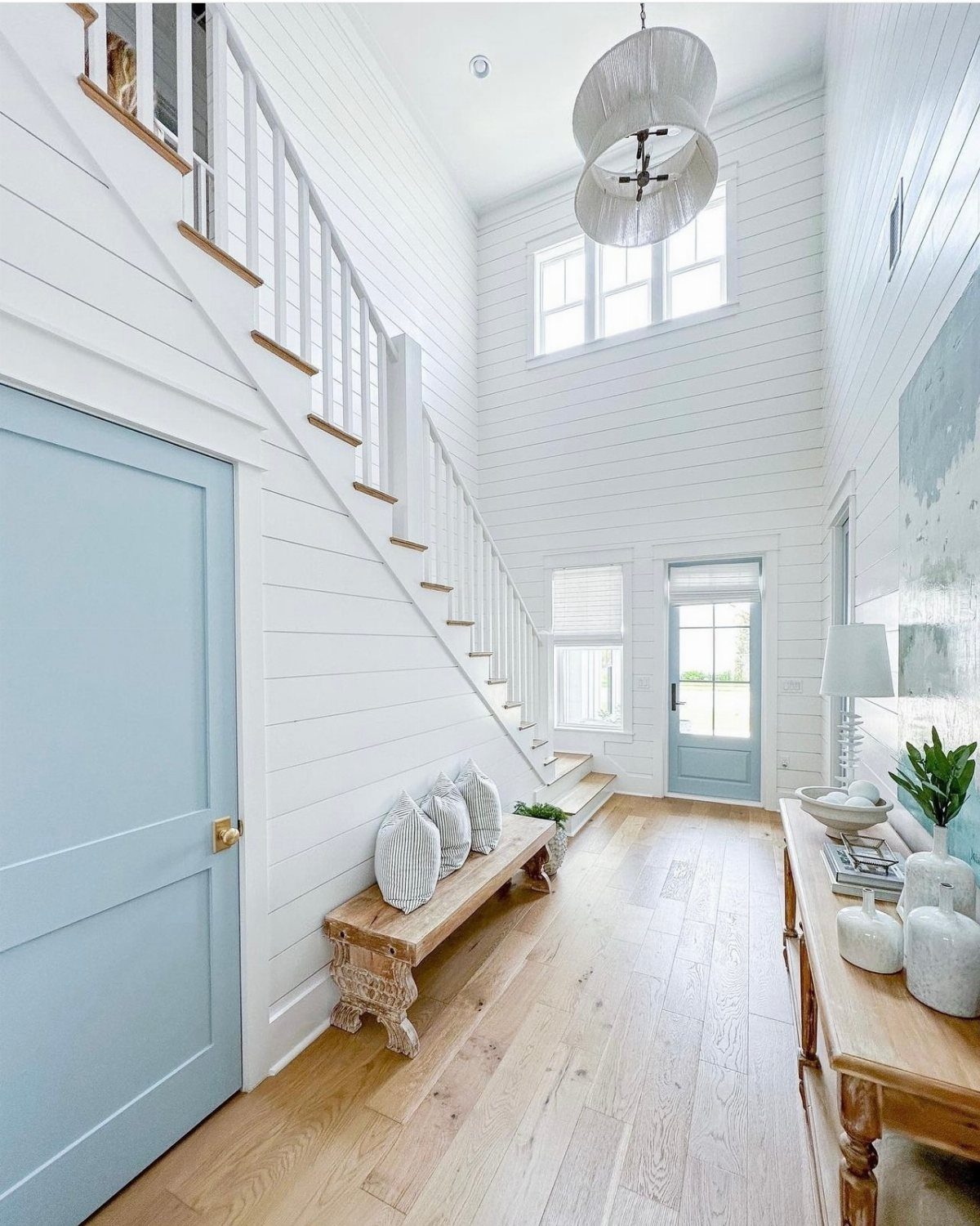 Bright hallway with white shiplap walls, light blue door, and wooden furniture.