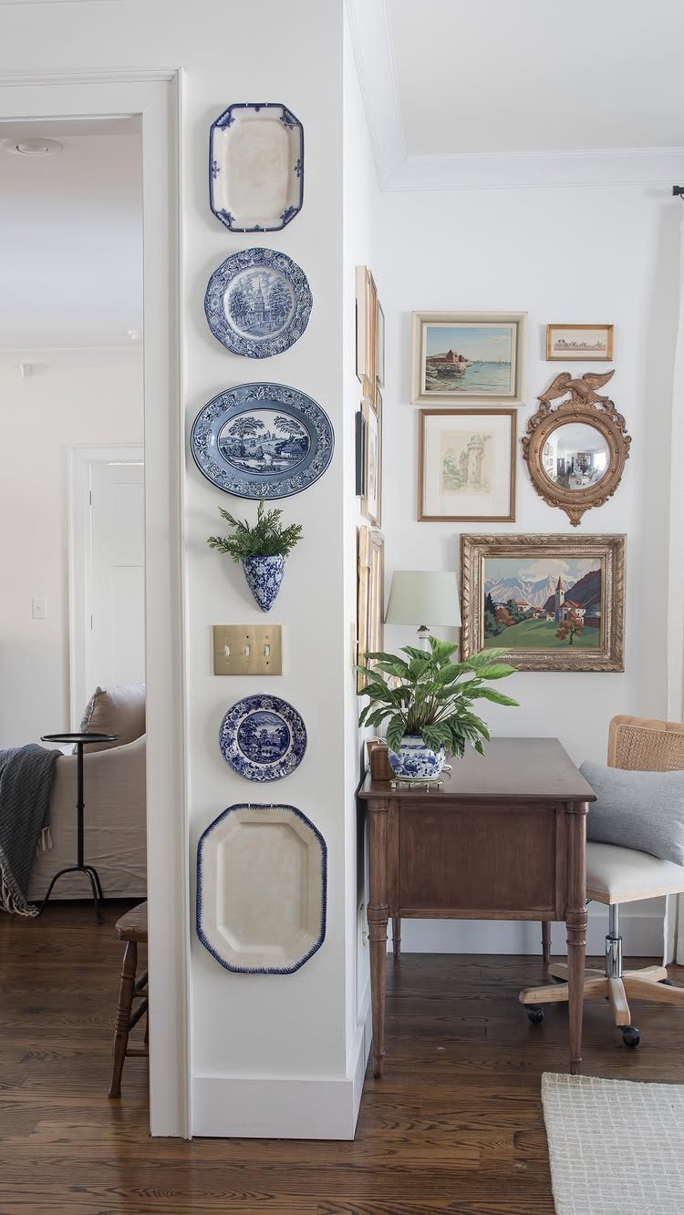 Blue and white ceramic plates and platters arranged vertically on a white hallway wall.