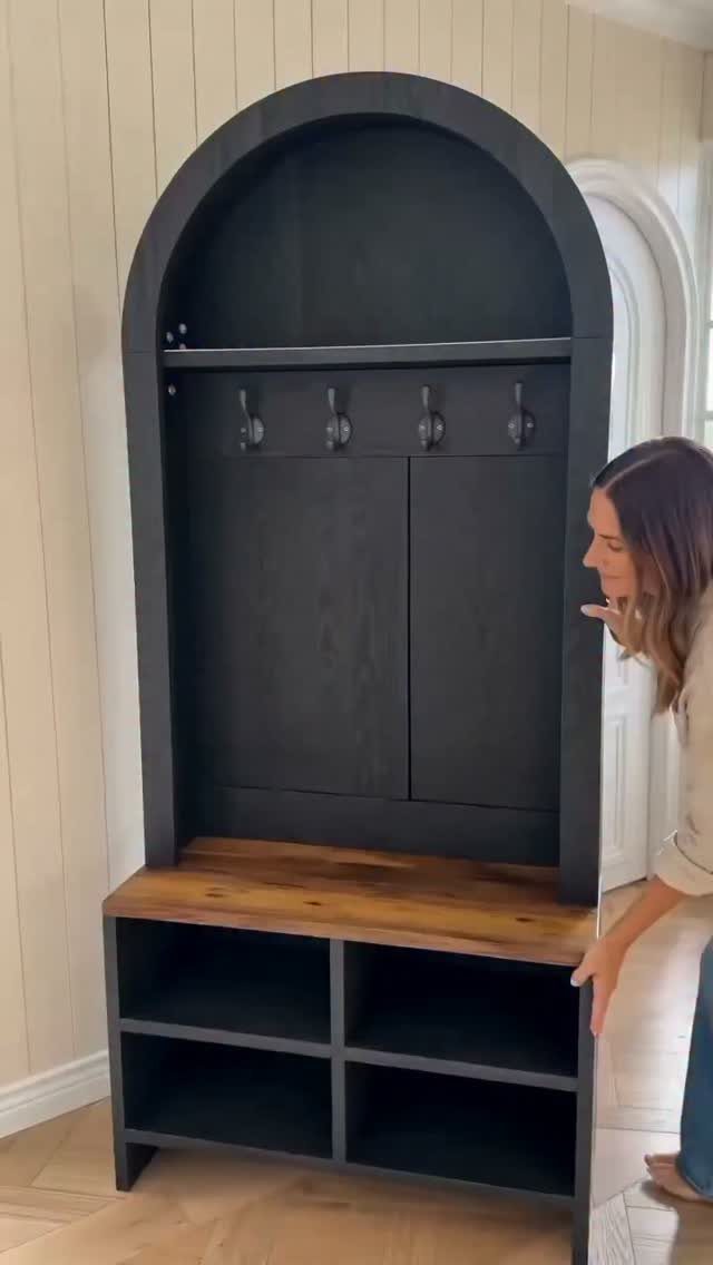 Dark grey arched entryway organizer with a wooden bench and storage cubbies against a paneled wall.