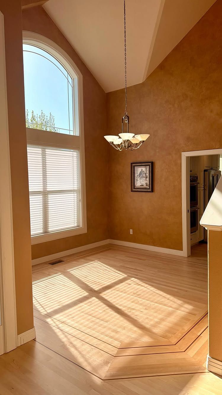 Light hardwood floors with an inlaid border pattern in a sunlit room with ochre walls.