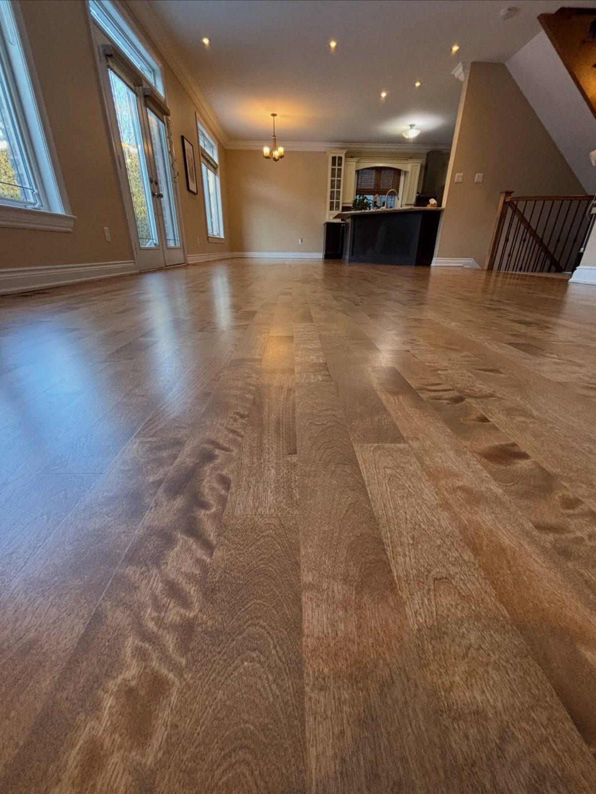 Polished medium-toned hardwood flooring stretching across a bright, spacious living room with large windows.