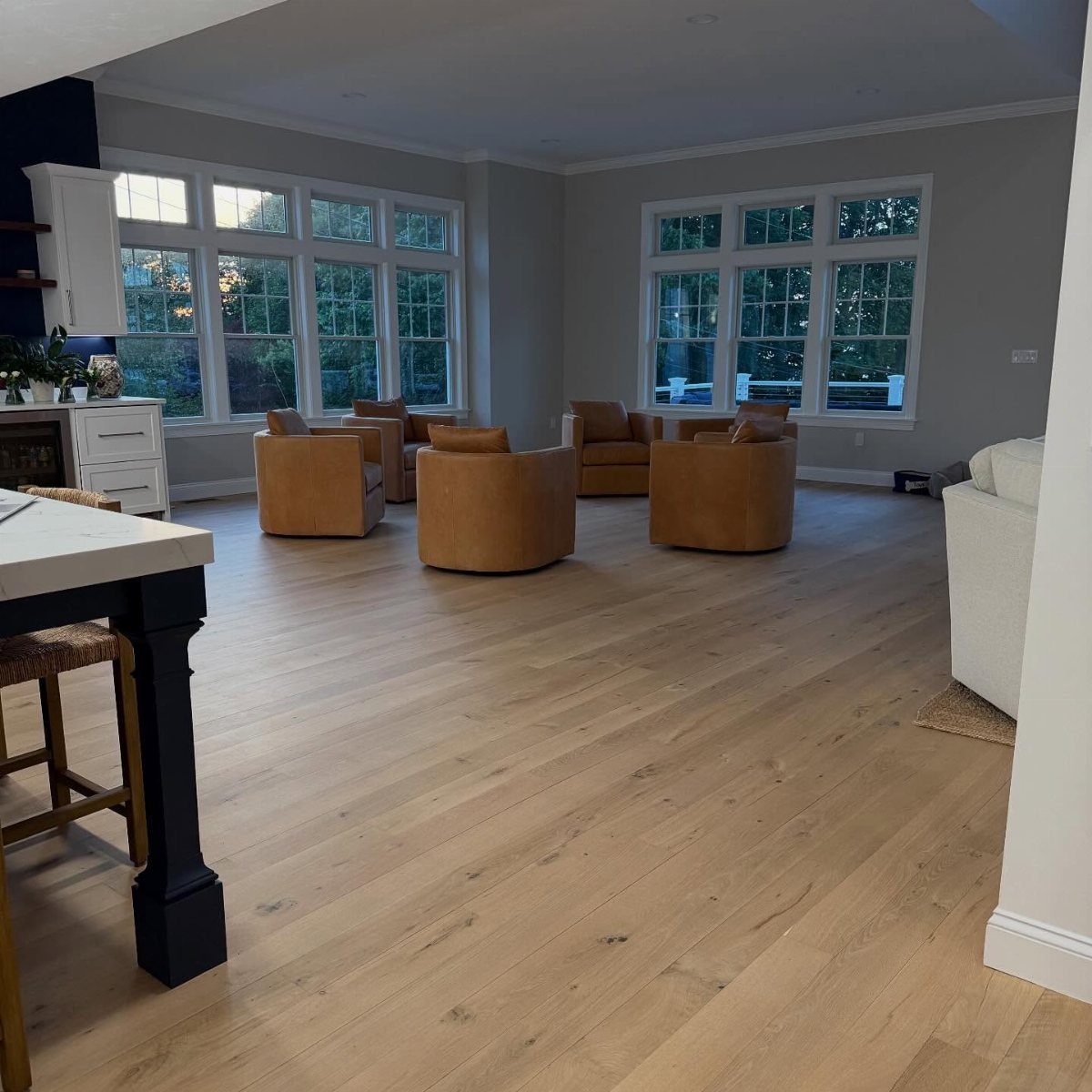 Light wood wide plank flooring in a bright, modern living room with leather armchairs.