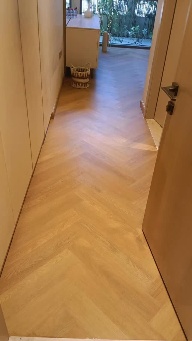 Light oak herringbone wooden floor extending through a narrow hallway toward a bright doorway.