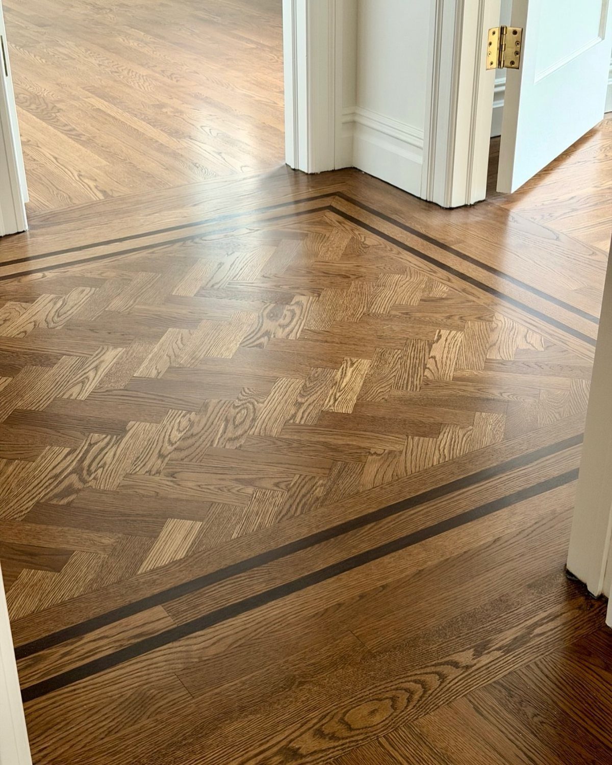 Polished wooden floor with a central herringbone pattern bordered by dark wood inlay strips.