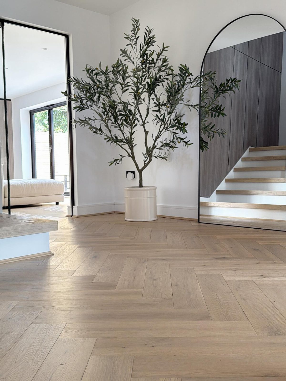 Light wood herringbone flooring in a bright, modern room with a potted olive tree.