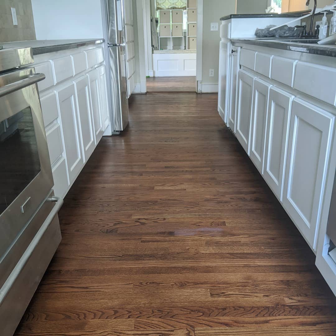 Medium-toned wooden plank flooring installed in a kitchen between white cabinets.