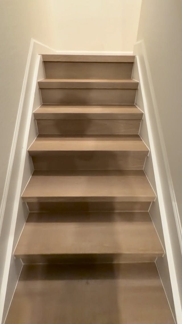 Light tan wooden stairs with white trim leading up between two off-white walls.
