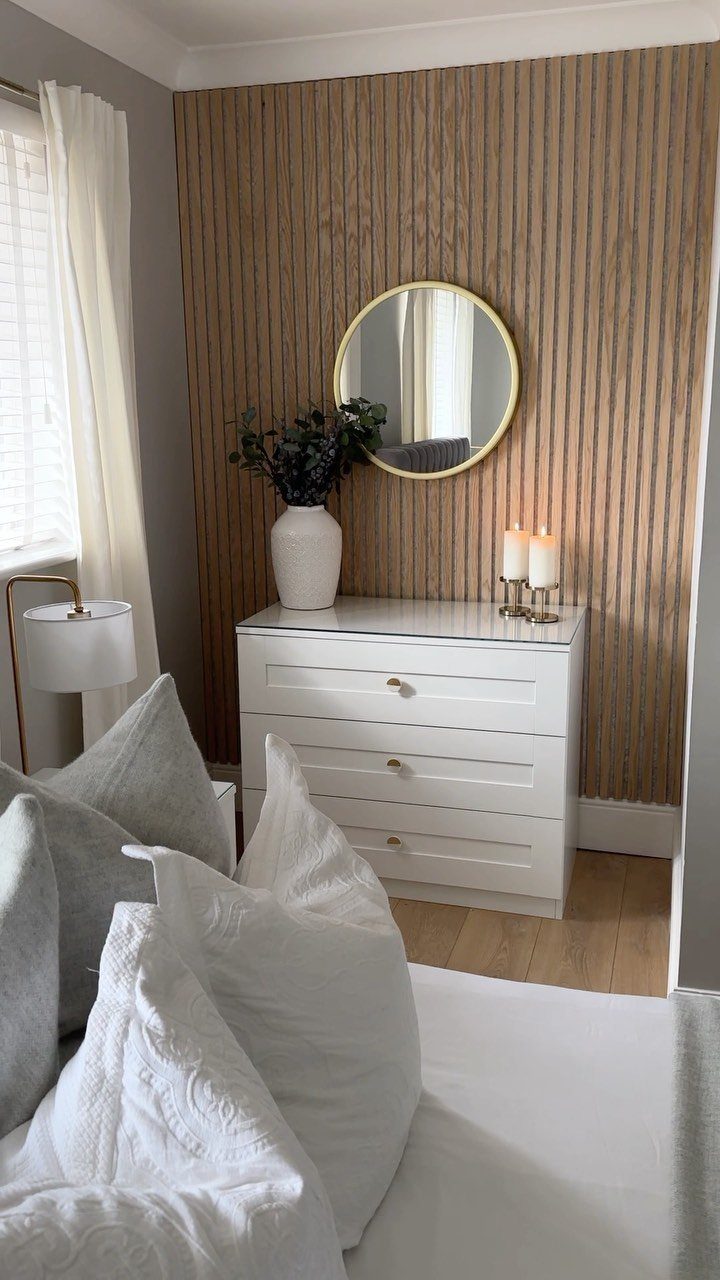 Vertical light oak wood slat accent wall behind a white dresser and round mirror.