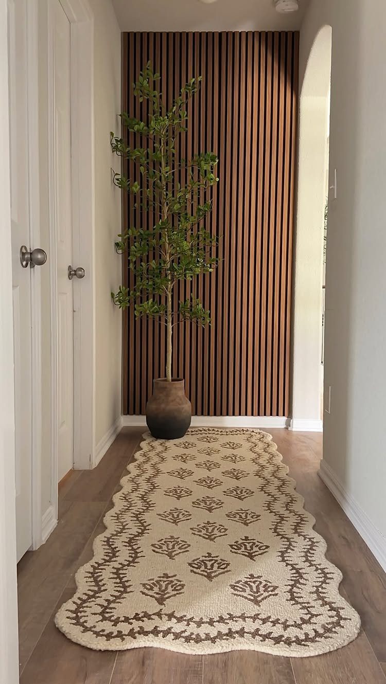 Vertical wooden slats form an accent wall behind a tall green plant in a hallway.