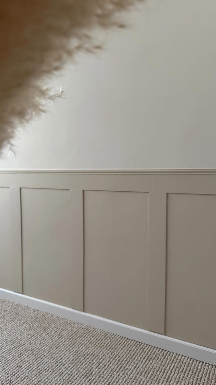 Beige wainscoting with rectangular recessed panels installed on a wall above grey carpet.