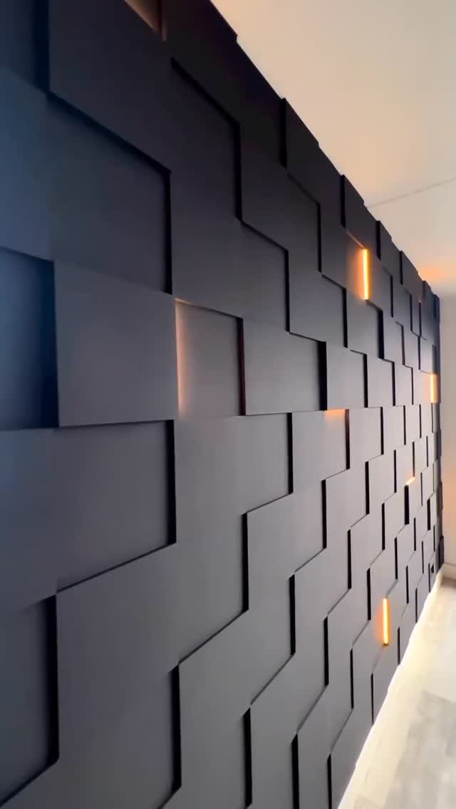 Dark grey geometric 3D wall panels with integrated warm orange accent lighting.