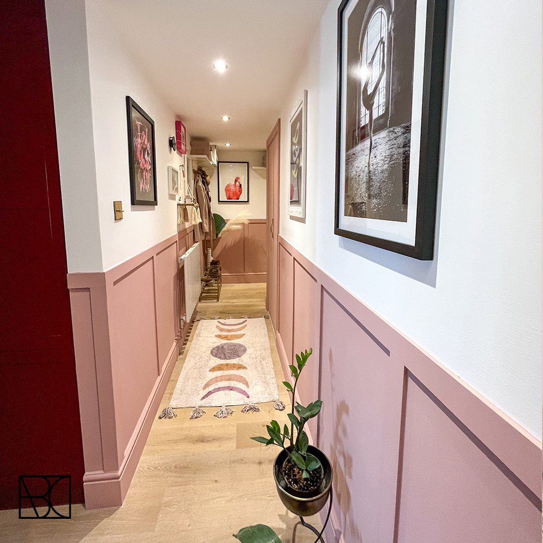 Pink painted wall paneling decorating the lower half of a narrow hallway with light wood floors.