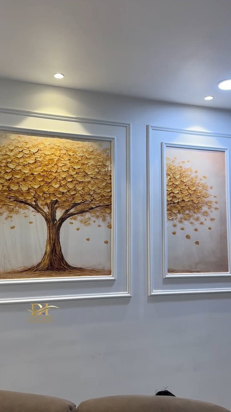 Two golden tree paintings framed by white decorative picture moulding on a grey wall.