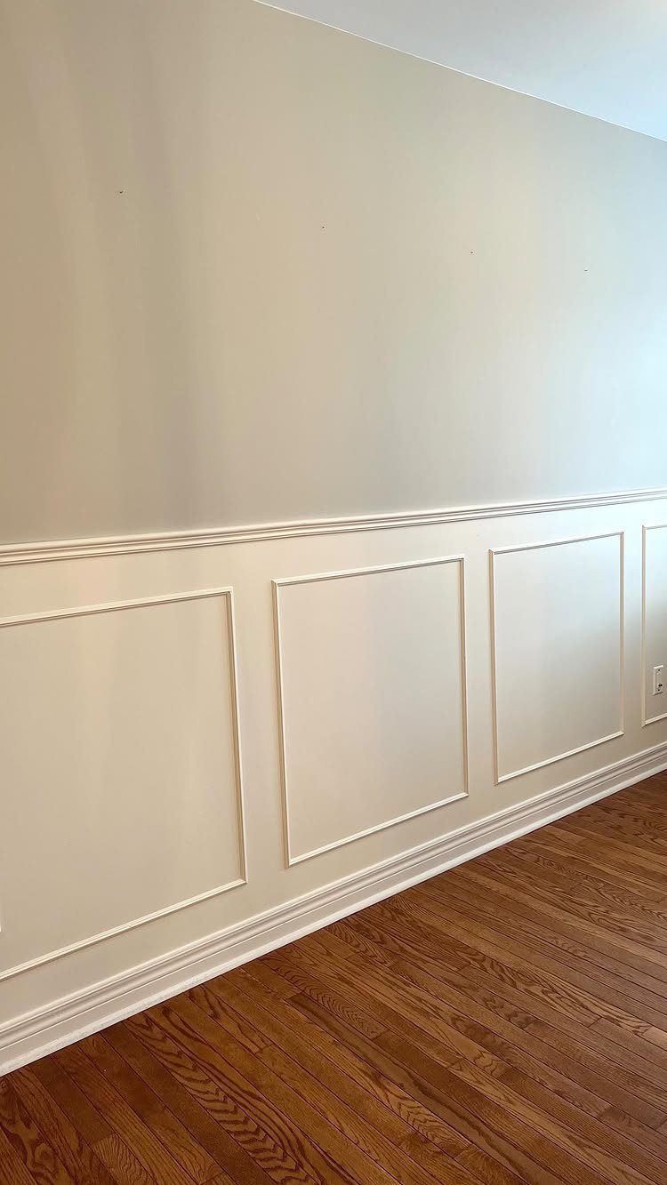 Decorative beige picture moulding panels installed on a lower wall above hardwood flooring.