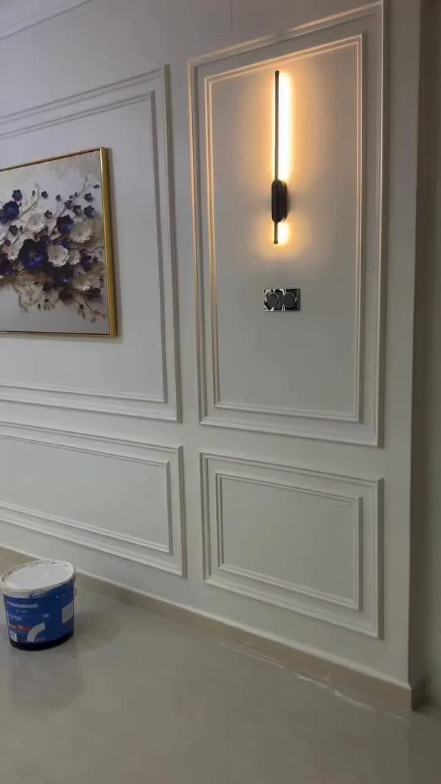 White decorative wall moulding panels featuring a glowing wall sconce and a floral painting.