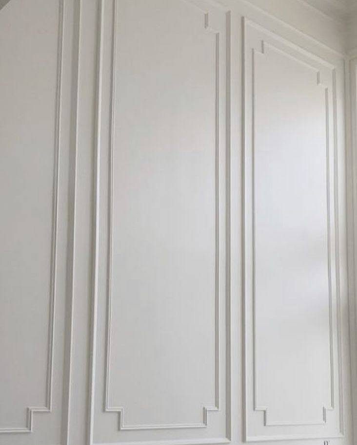 White decorative wall panels featuring elegant picture moulding with stepped corner details on a bright wall.