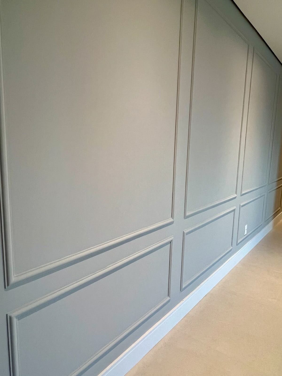 Light blue walls decorated with rectangular picture moulding panels and white baseboards.