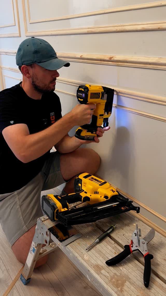 Man using a yellow cordless nail gun to install wooden molding strips onto a wall.