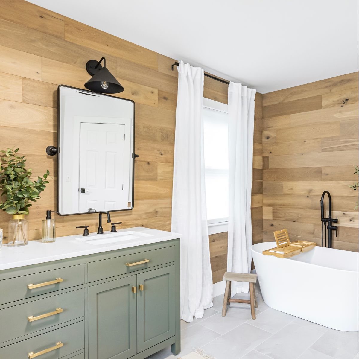 Modern bathroom with light wood paneled walls, a white bathtub, and a sage green vanity.