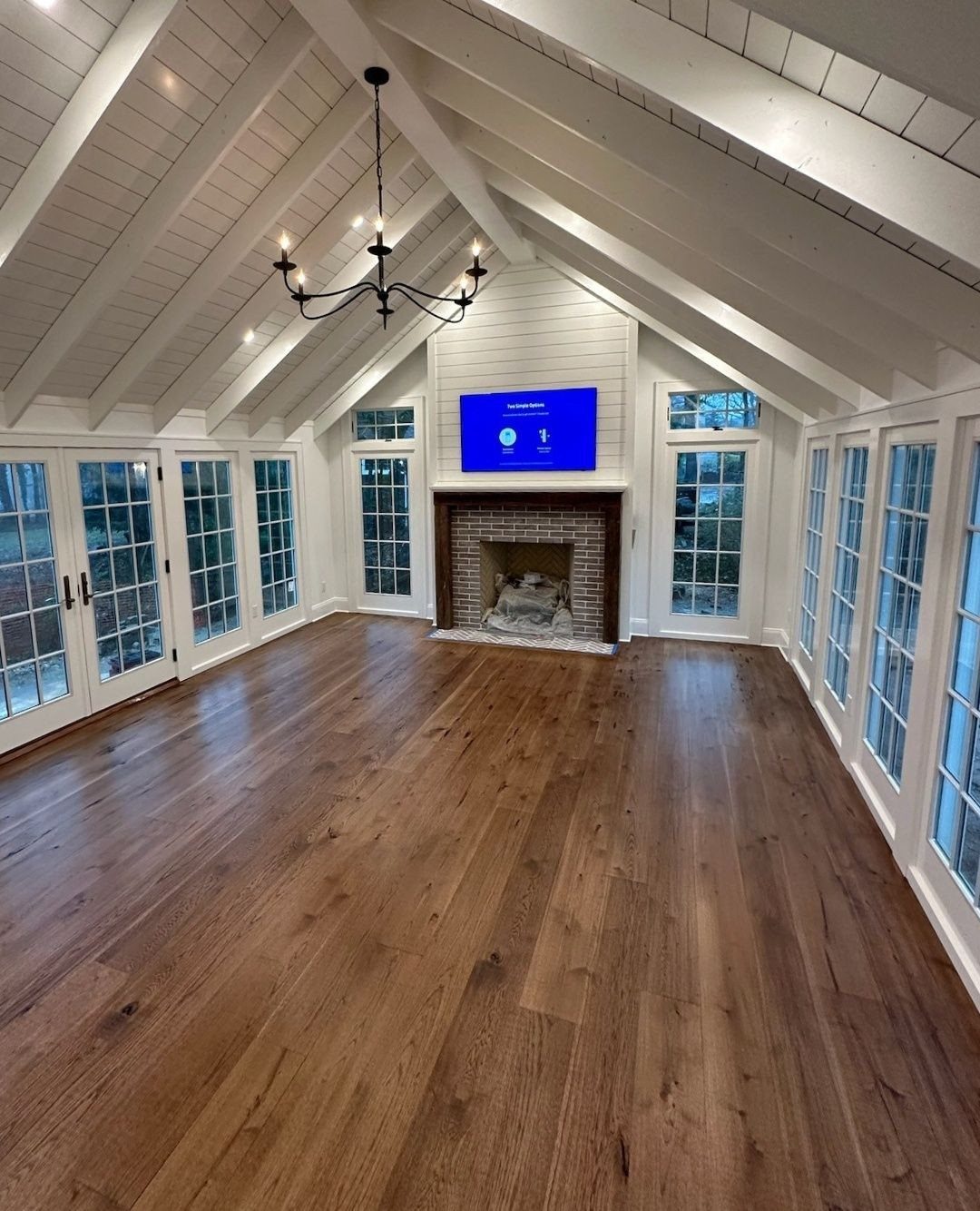 Wide medium-toned wood planks covering the floor of a bright room with vaulted ceilings.