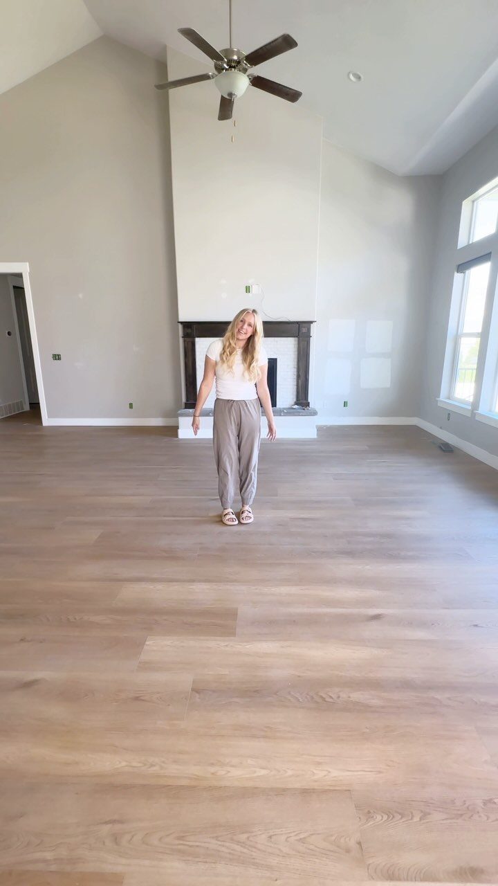 A woman standing in a spacious room with light-colored wide plank wood flooring.