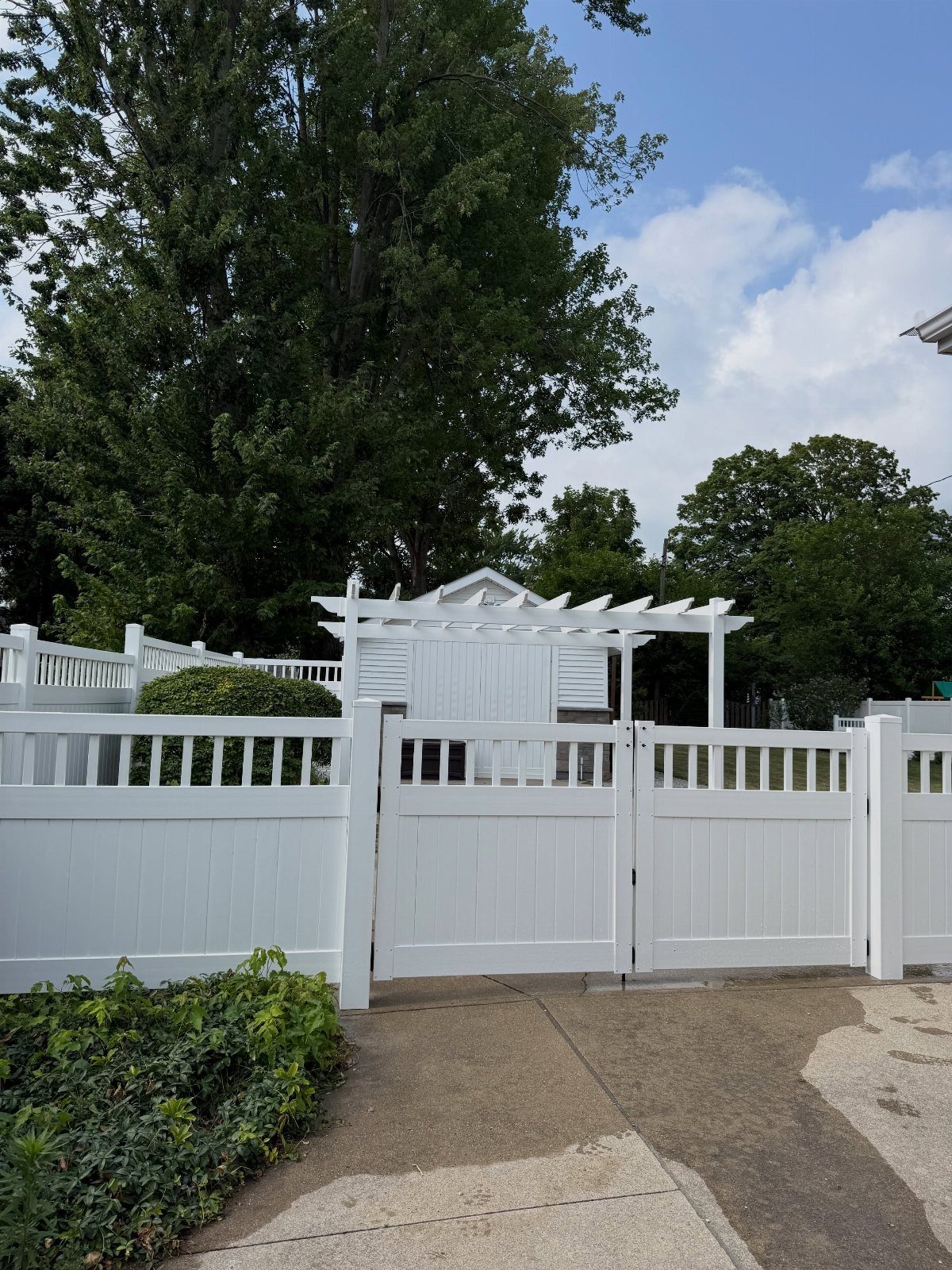 White vertical slat vinyl privacy fence with a matching gate and pergola structure in a yard.