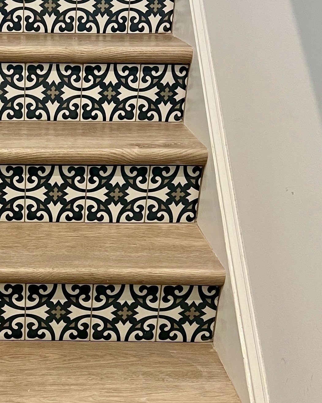 Wooden stairs featuring decorative black and white patterned tile risers against a white wall.
