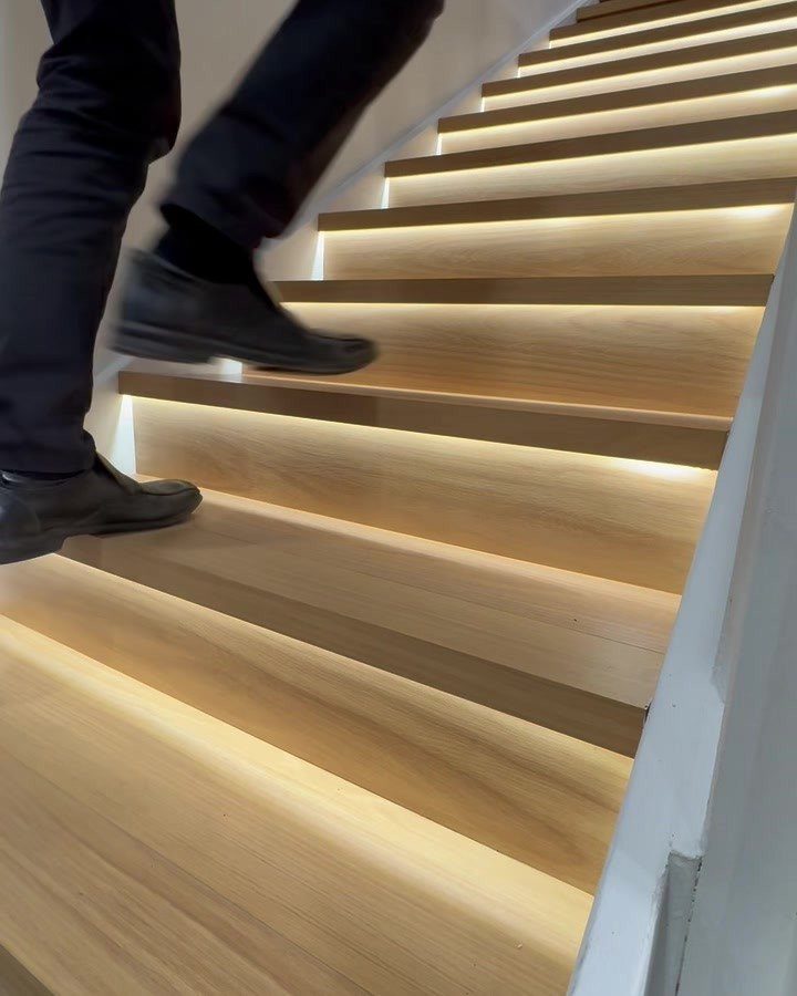 Person walking up wooden stairs featuring integrated warm LED strip lighting under each step.