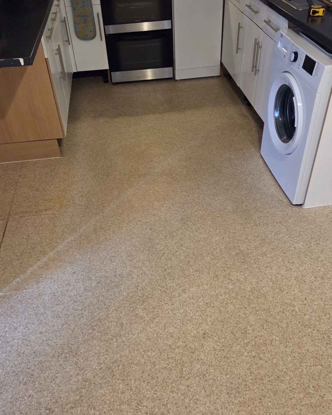 Beige textured vinyl flooring installed in a kitchen with white cabinets and appliances.