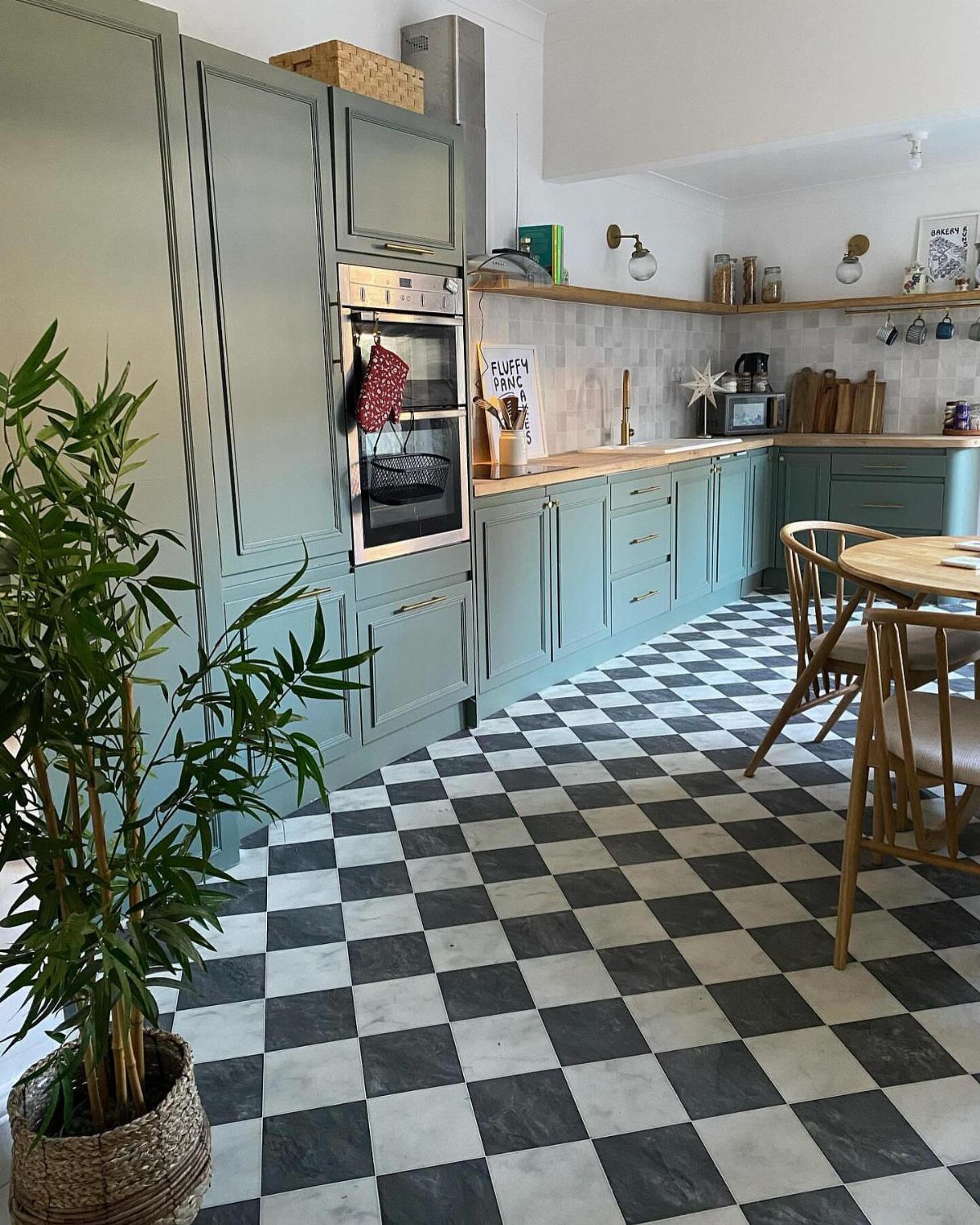 Black and white checkerboard patterned vinyl flooring in a sage green kitchen with wooden furniture.
