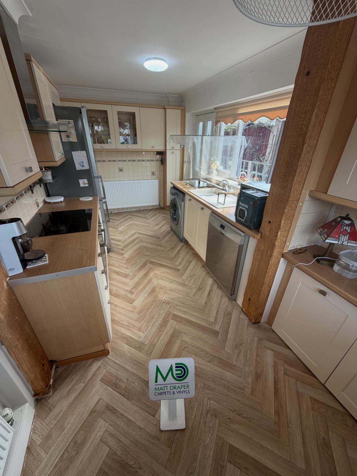 Light wood-effect vinyl flooring in a herringbone pattern installed in a kitchen setting.