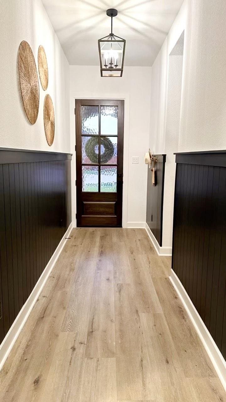 Dark wood wainscoting lines a narrow entryway with light wood floors and a glass door.