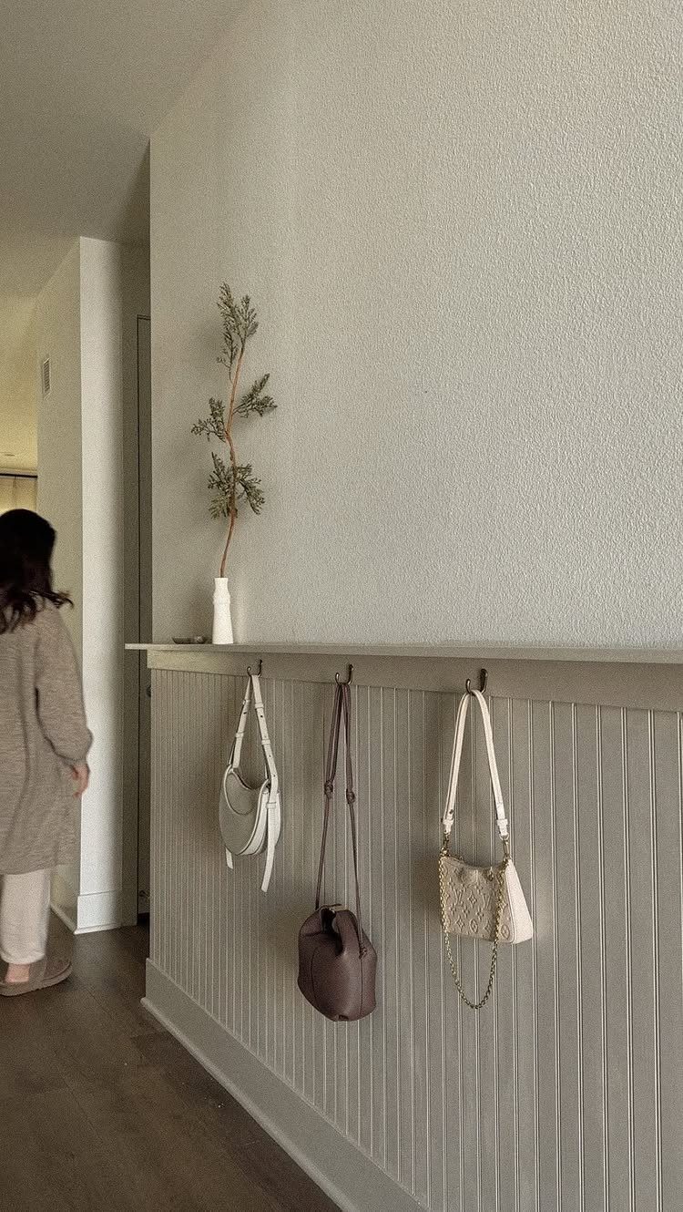 Vertical beadboard wainscoting in a grey entryway with hanging handbags and a small vase.