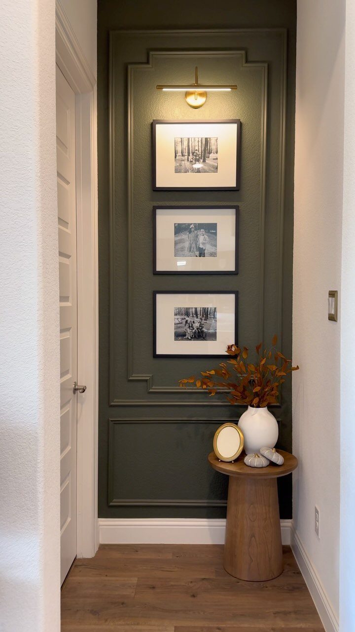 Olive green entryway wall with decorative picture frame molding and three framed black and white photos.