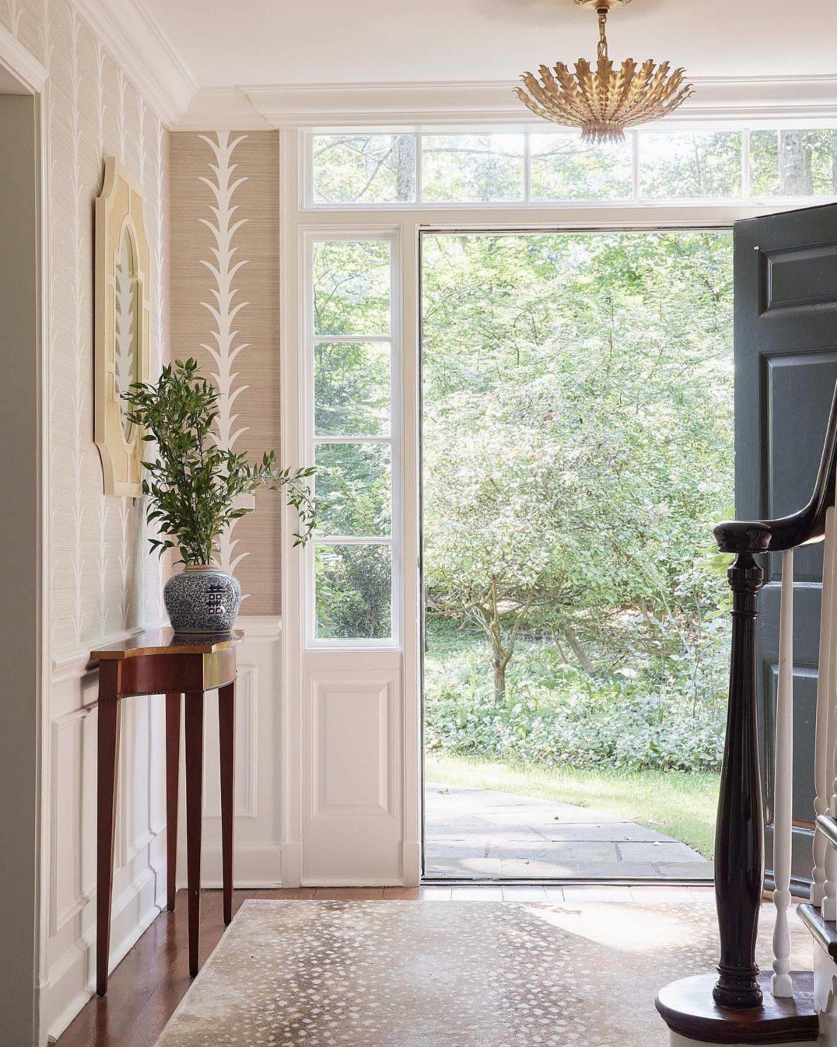 White wainscoting and patterned beige wallpaper in a bright, sunlit entryway with an open door.