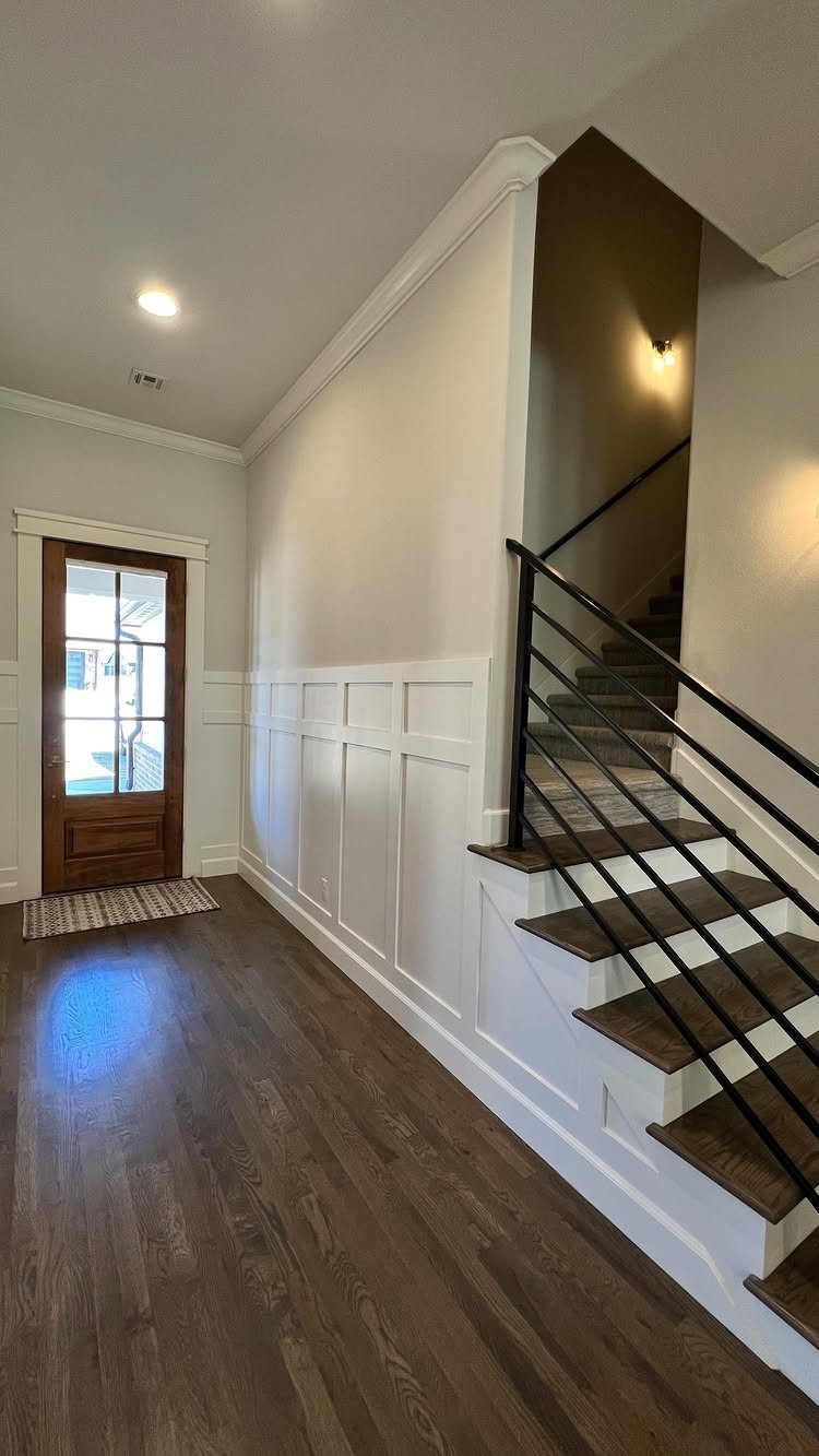 White board and batten wainscoting installed in a bright entryway with dark wood floors.