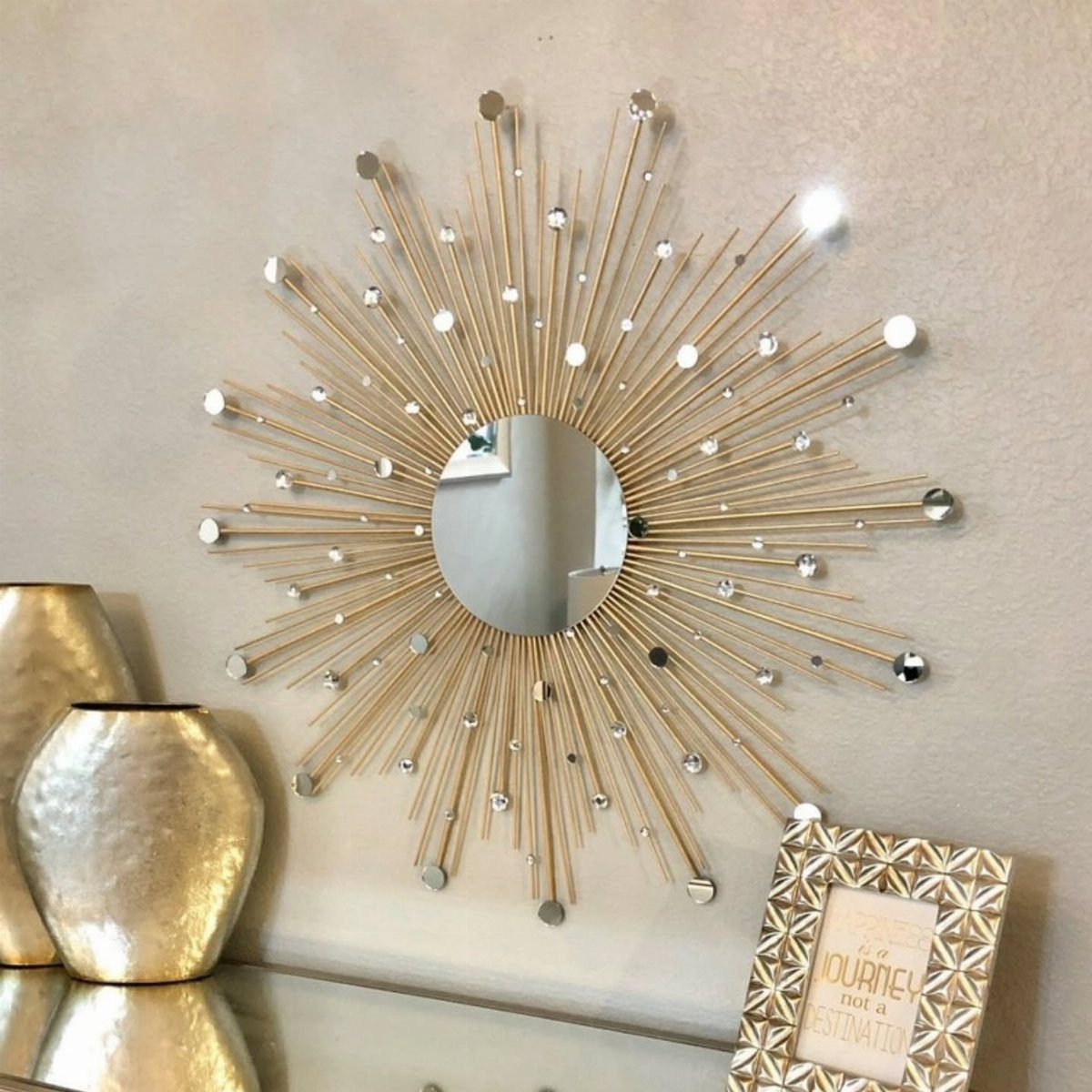 14 Wall Design in Living Room Ideas That Add Real Depth 1 A gold sunburst mirror with crystal accents hangs on a beige wall above gold vases.