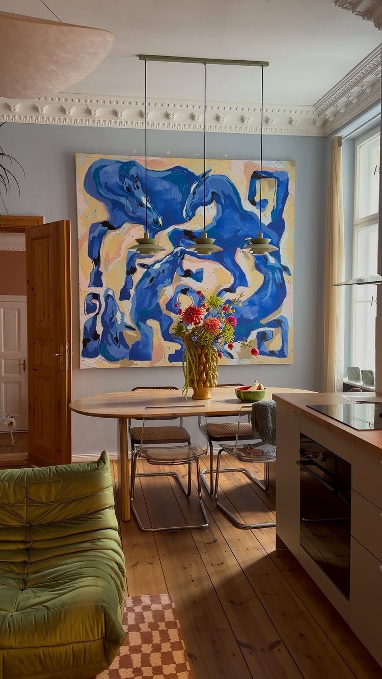14 Wall Design in Living Room Ideas That Add Real Depth 5 Large abstract blue painting hanging on a light blue wall above a wooden dining table.