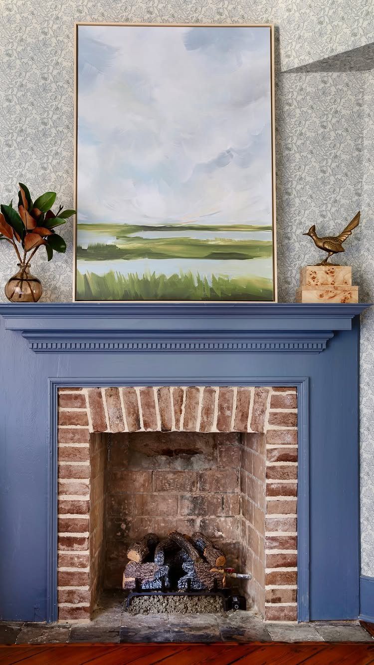 14 Wall Design in Living Room Ideas That Add Real Depth 9 Large landscape painting resting on a blue mantelpiece above a brick fireplace.
