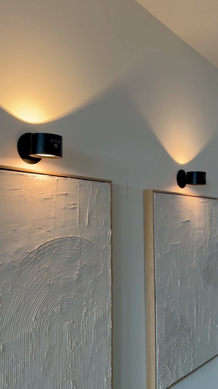 14 Wall Design in Living Room Ideas That Add Real Depth 6 Black cylindrical wall sconces illuminating textured white abstract art on a light wall.