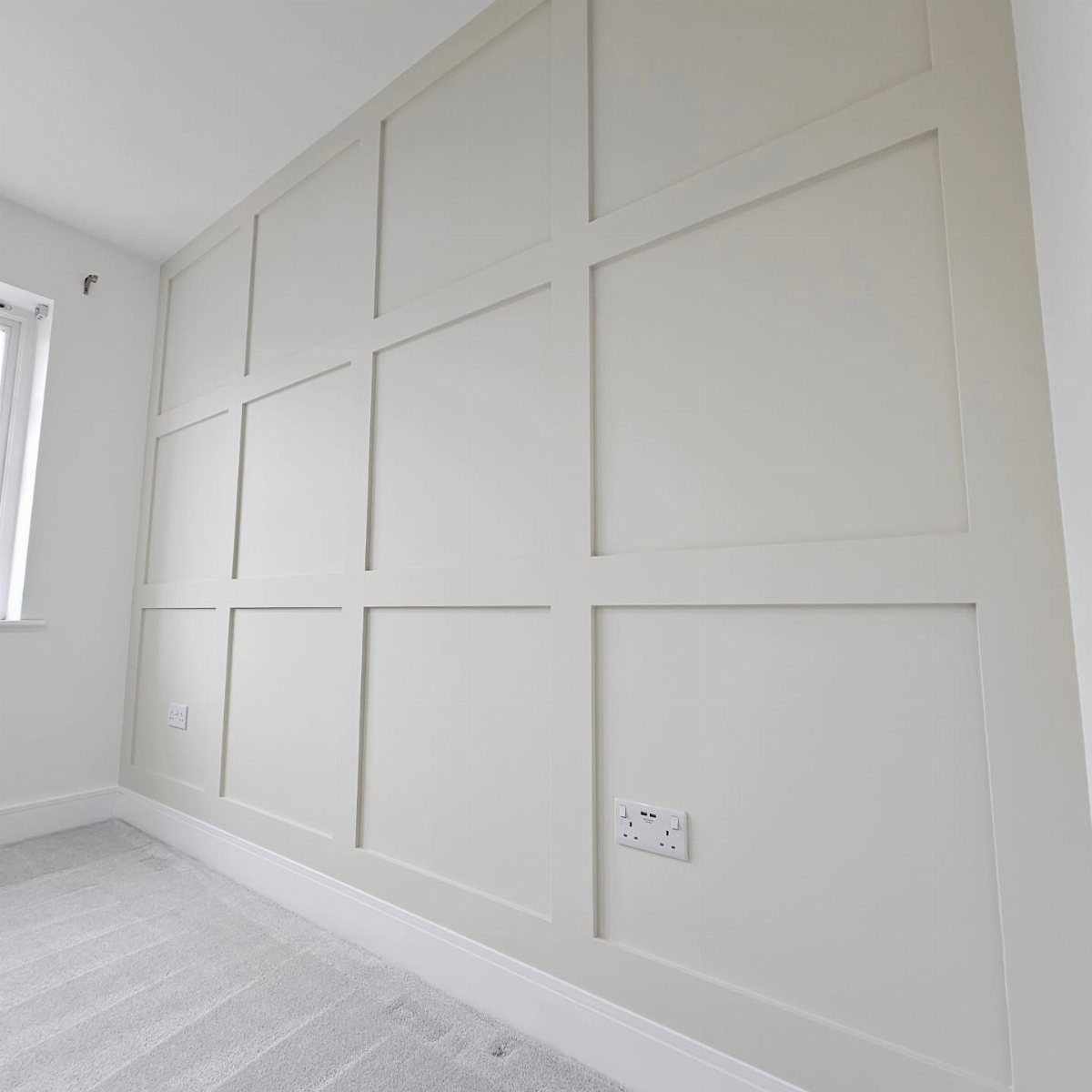 White wall with large rectangular box trim moulding and light grey carpeted floor.