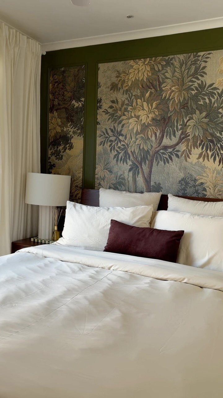 Botanical patterned fabric panels mounted on a dark green accent wall behind a white bed.