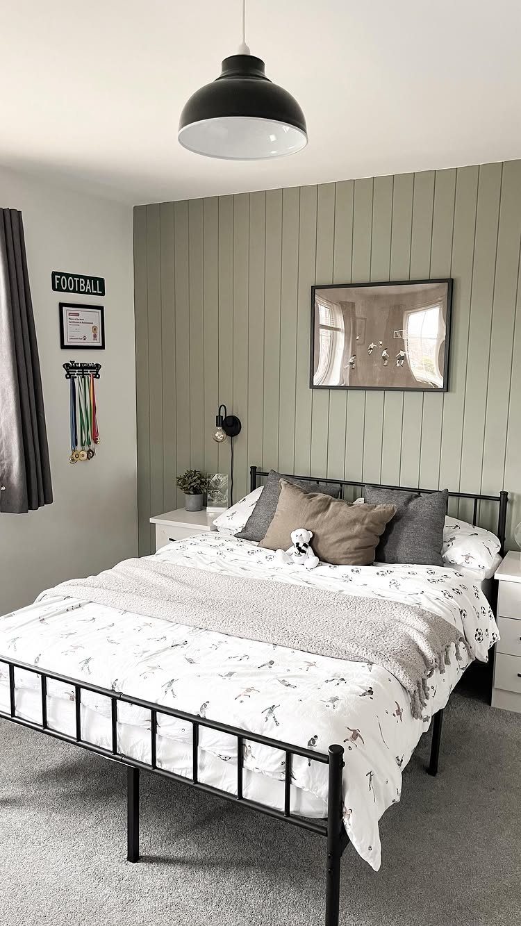 A bedroom with a sage green tongue and groove wood paneled accent wall and black metal bed.